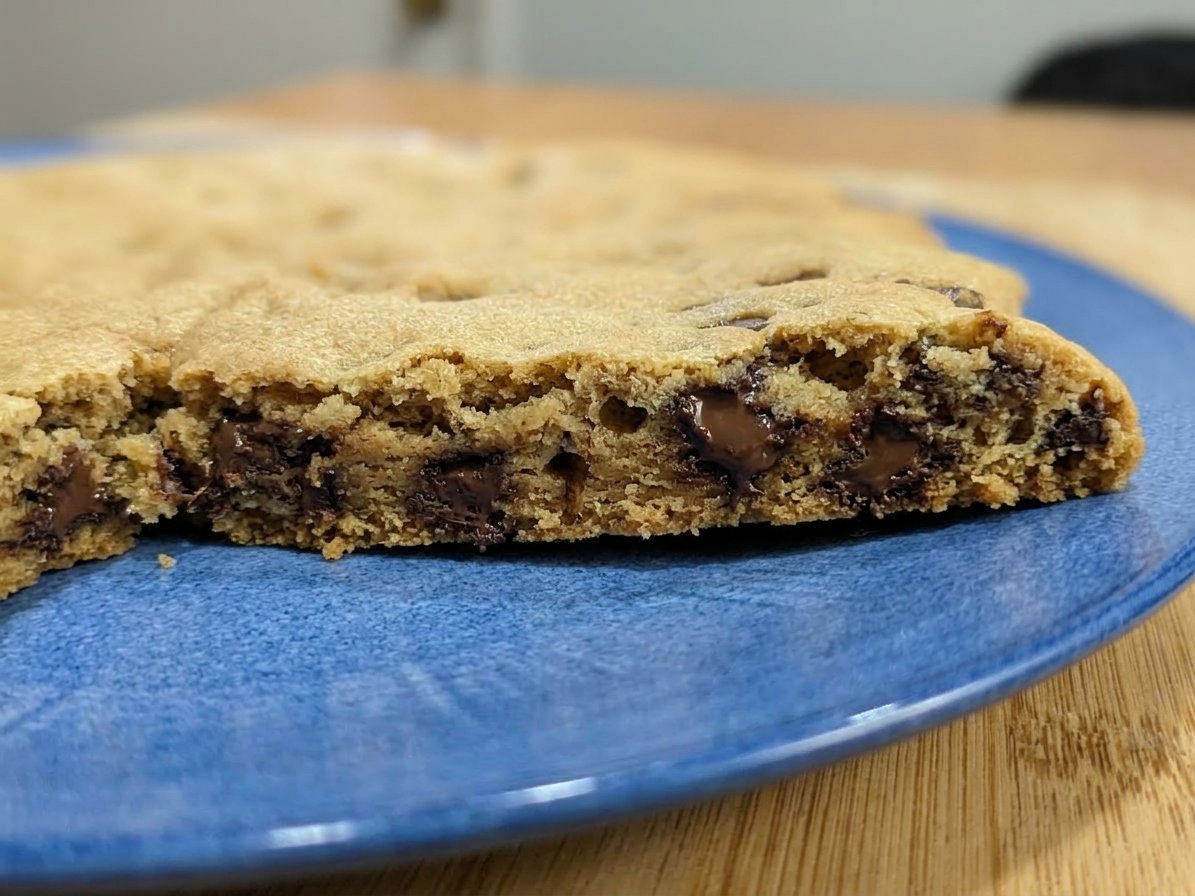 A collection of golden brown crispy chocolate chip cookies inside a vintage glass jar.