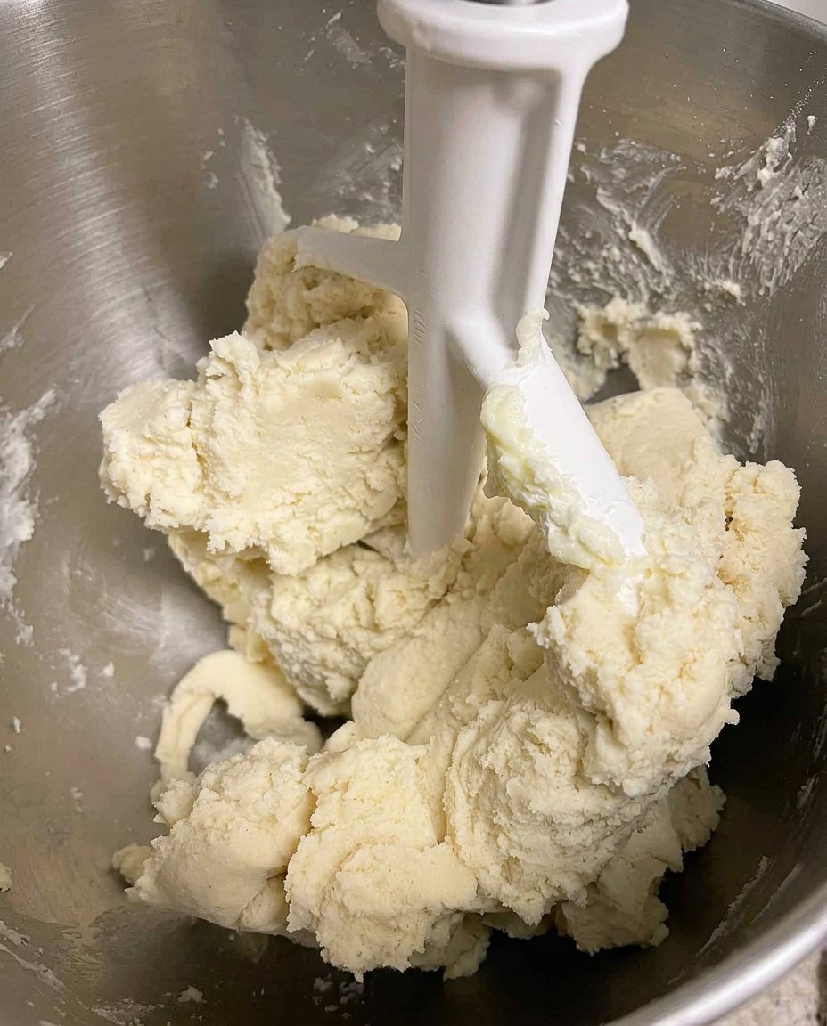 A vintage cookie press squeezing star-shaped dough onto a silicone baking mat